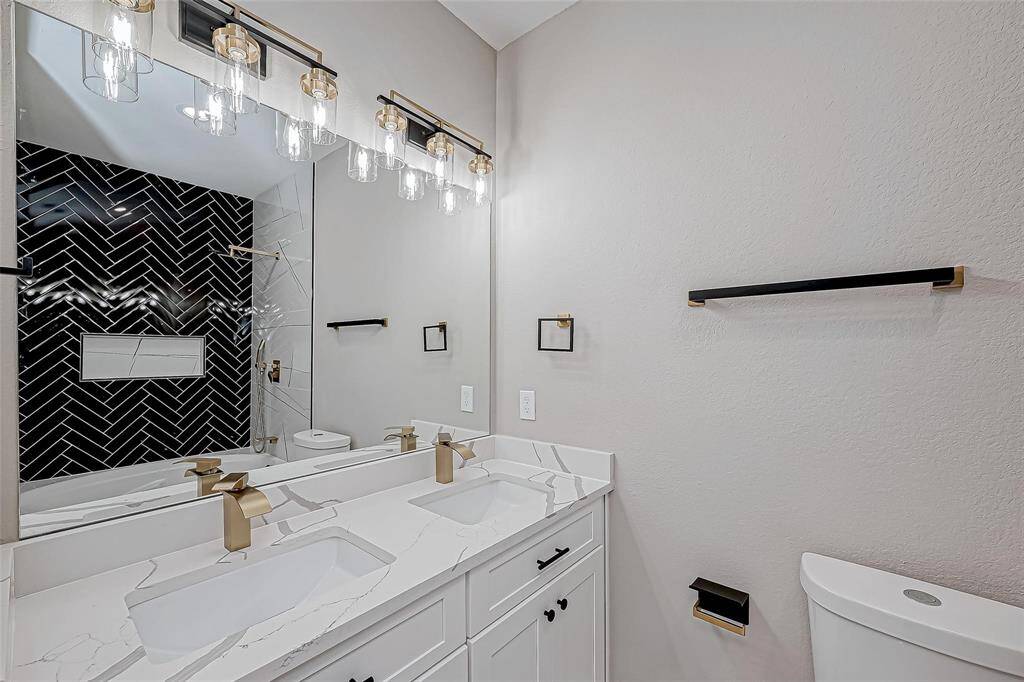Modern bathroom with dual sinks, elegant marble countertops, and sleek brass fixtures. Features a striking black herringbone tile design in the shower area, complemented by stylish lighting.