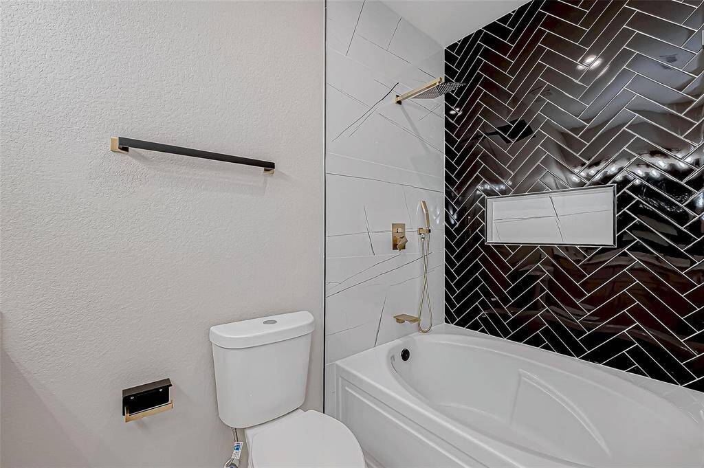 Modern bathroom with a sleek design featuring a white tub, black herringbone tile accent wall, and gold fixtures.