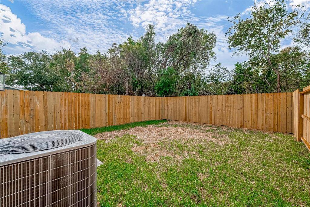 Cozy backyard featuring a wooden privacy fence and a grassy area, perfect for outdoor activities. An air conditioning unit is visible, indicating modern amenities. Relaxing space with a backdrop of trees for added privacy.