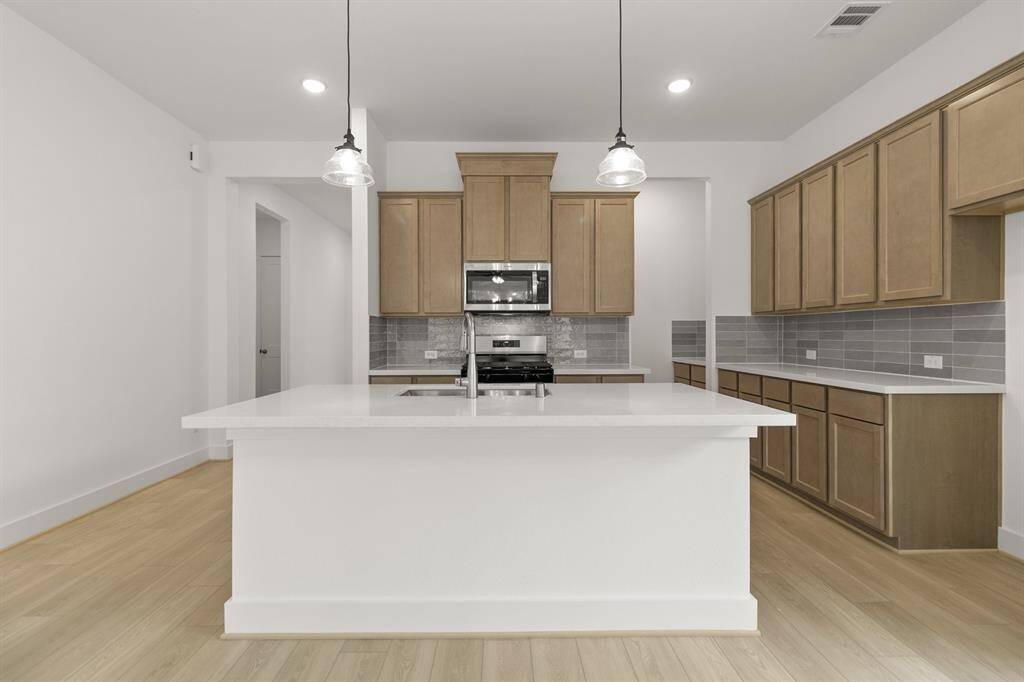 The spacious open-concept kitchen is a perfect blend of warmth and modern style, featuring rich brown cabinets and sleek white quartz countertops that offer both elegance and functionality.