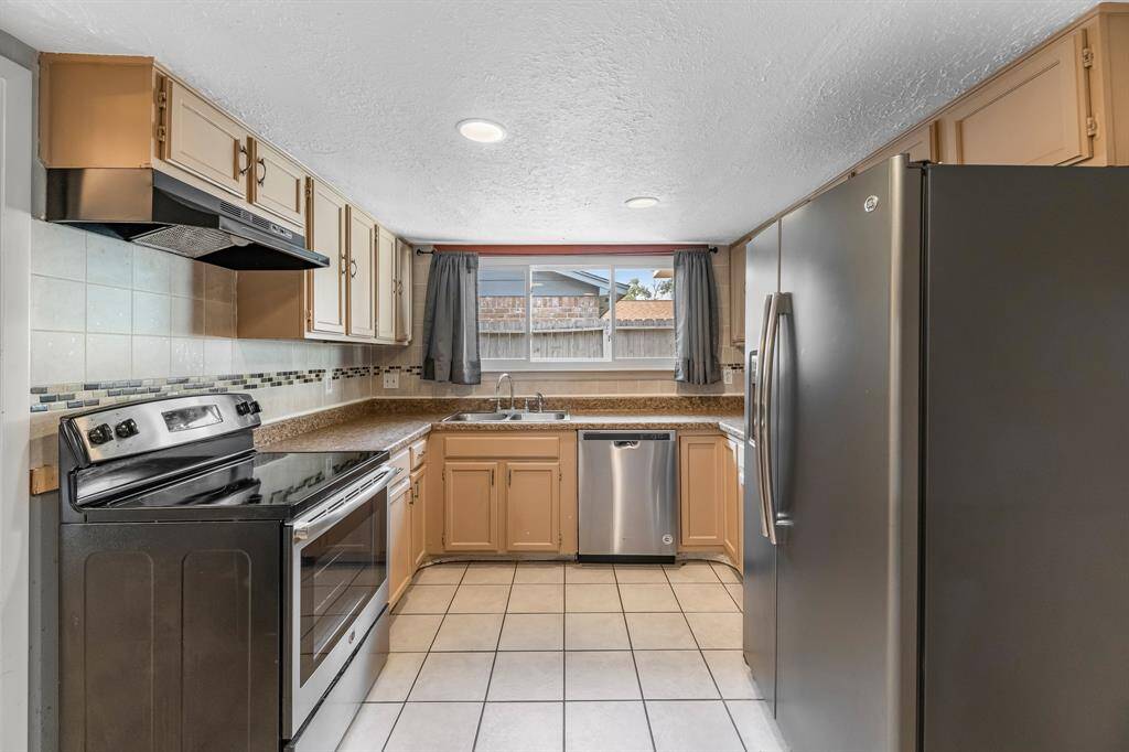 This light and bright kitchen features light stained cabinets, a large sink overlooking the backyard, recessed lighting, and beautiful backsplash.