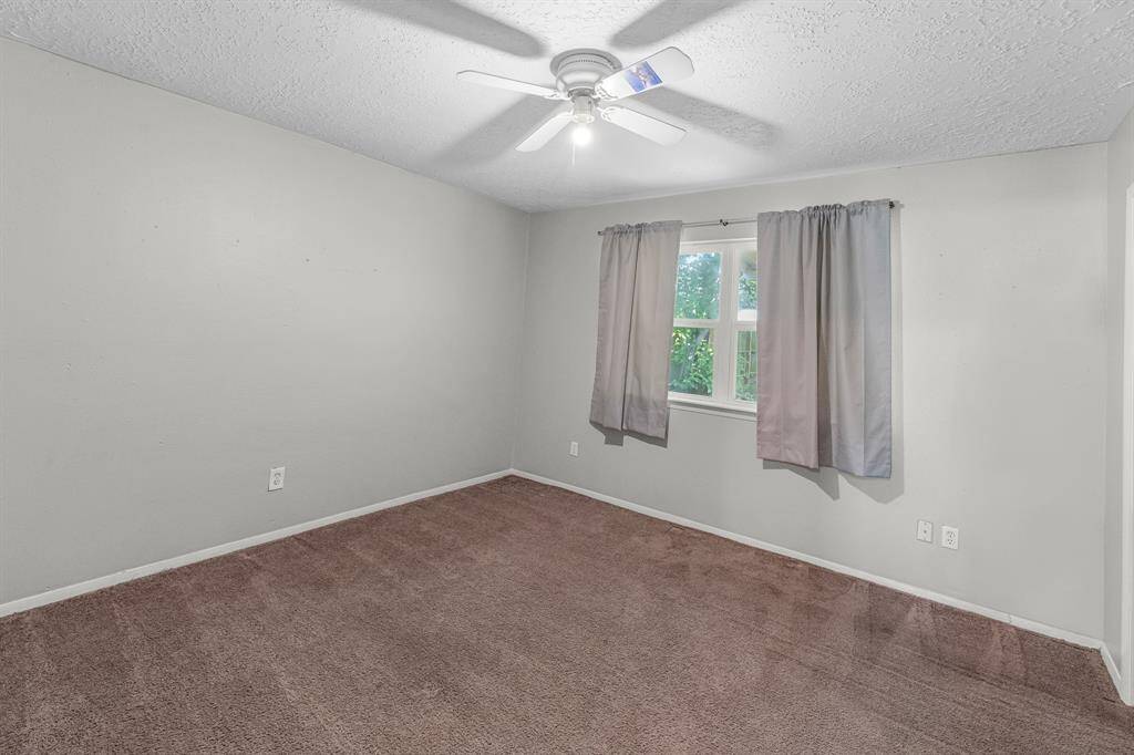 Spacious secondary bedroom featuring a large window, plush carpet, neutral paint tones, and a ceiling fan with lighting—comfortable and move-in ready.