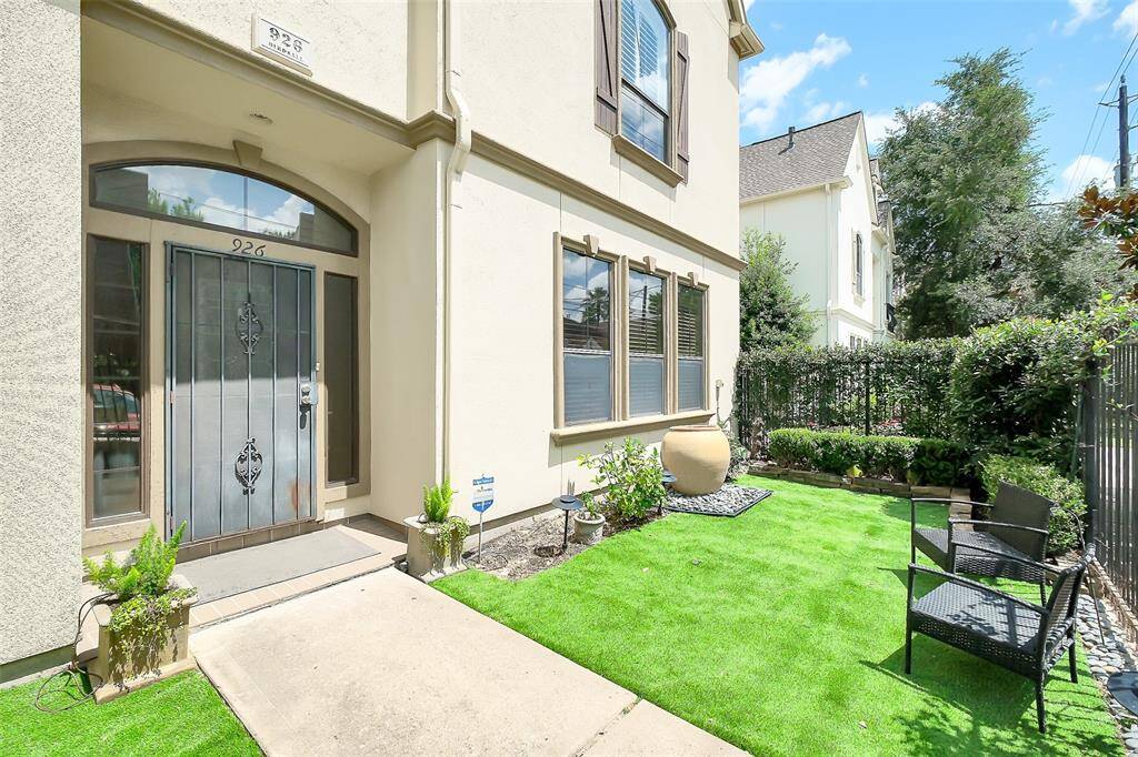 Charming townhouse with a stucco exterior, featuring a gated entry and manicured landscaping. The driveway leads to a private garage.