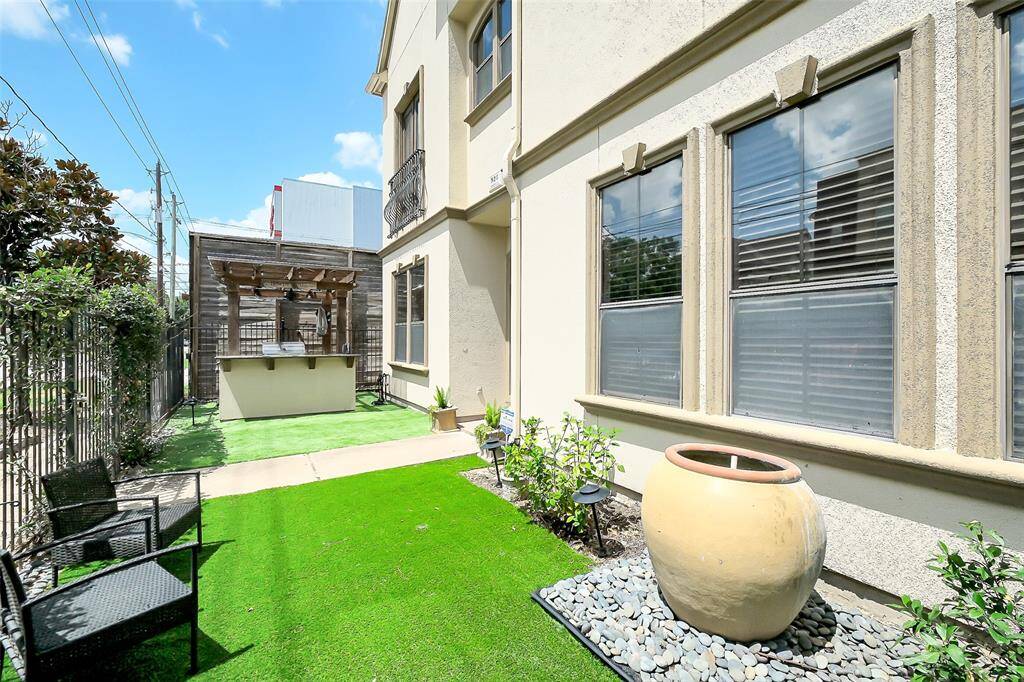 Charming backyard area featuring a cozy outdoor seating space, lush artificial turf, and a stylish pergola with a built-in bar. Perfect for entertaining or relaxing.