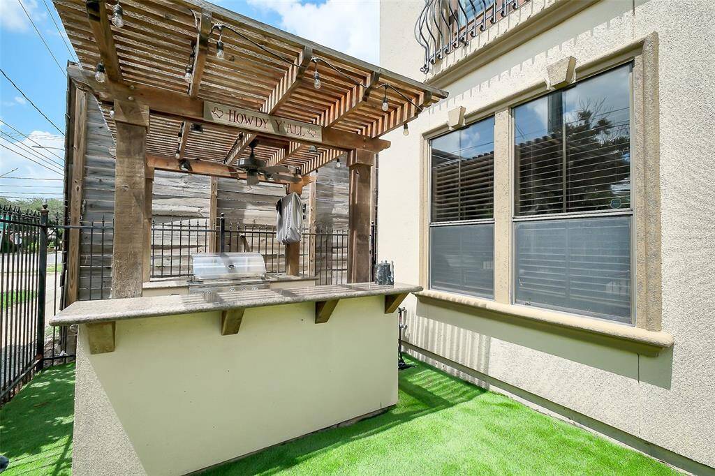 Charming outdoor space featuring a pergola with string lights, a built-in grill, and a countertop, perfect for entertaining. The area is fenced and has artificial grass for easy maintenance.
