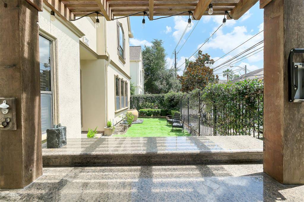 Fabulous side yard with a lush green lawn and seating area, bordered by a wrought iron fence and hedges creating a welcoming outdoor space with a modern, tranquil vibe.