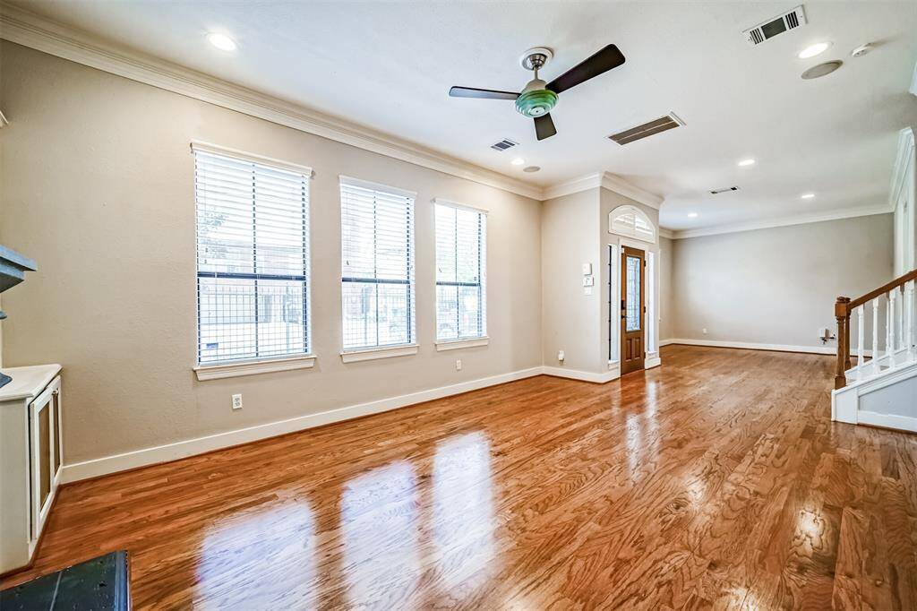 This inviting living room features elegant hardwood floors, a cozy fireplace with built-in shelving on either side, and ample natural light from three large windows. The ceiling fan adds comfort, making it a perfect space for relaxation and entertaining.