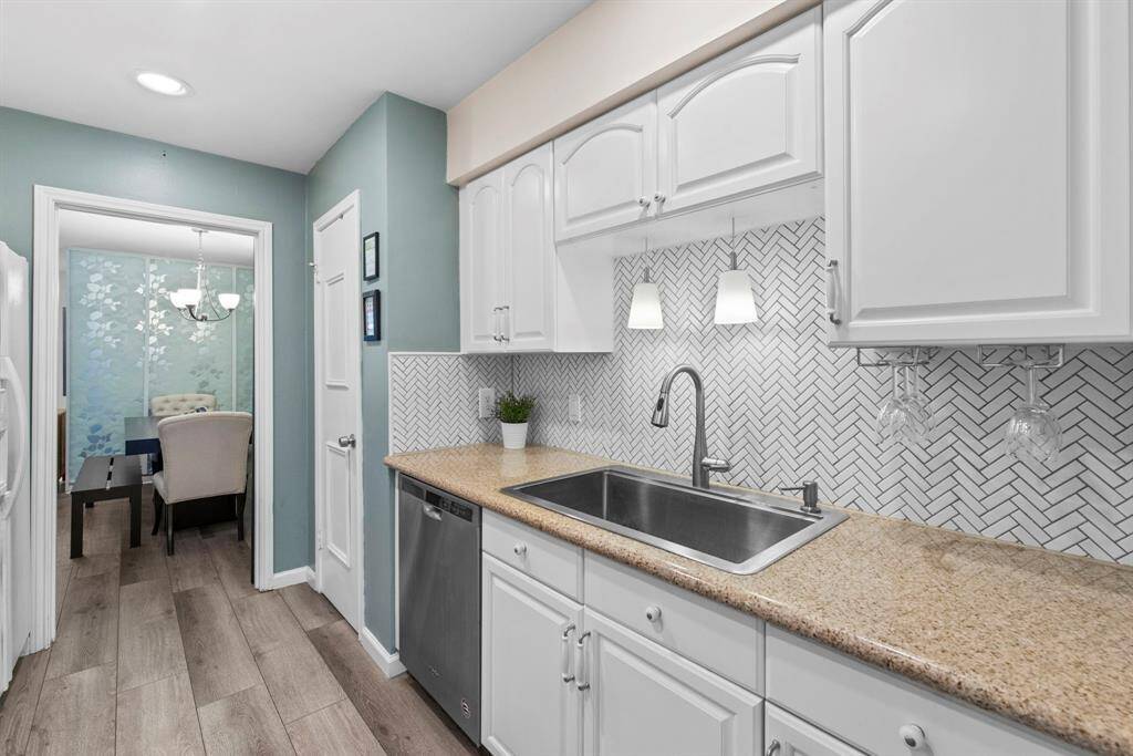 The galley kitchen is bright and functional, with granite counters, white cabinetry, and a chevron tile backsplash for added flair.