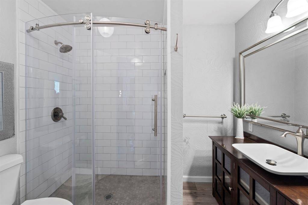 This refreshed ensuite bathroom features a walk-in shower with subway tile and glass enclosure, paired with a rich wood vanity and sleek modern sink.