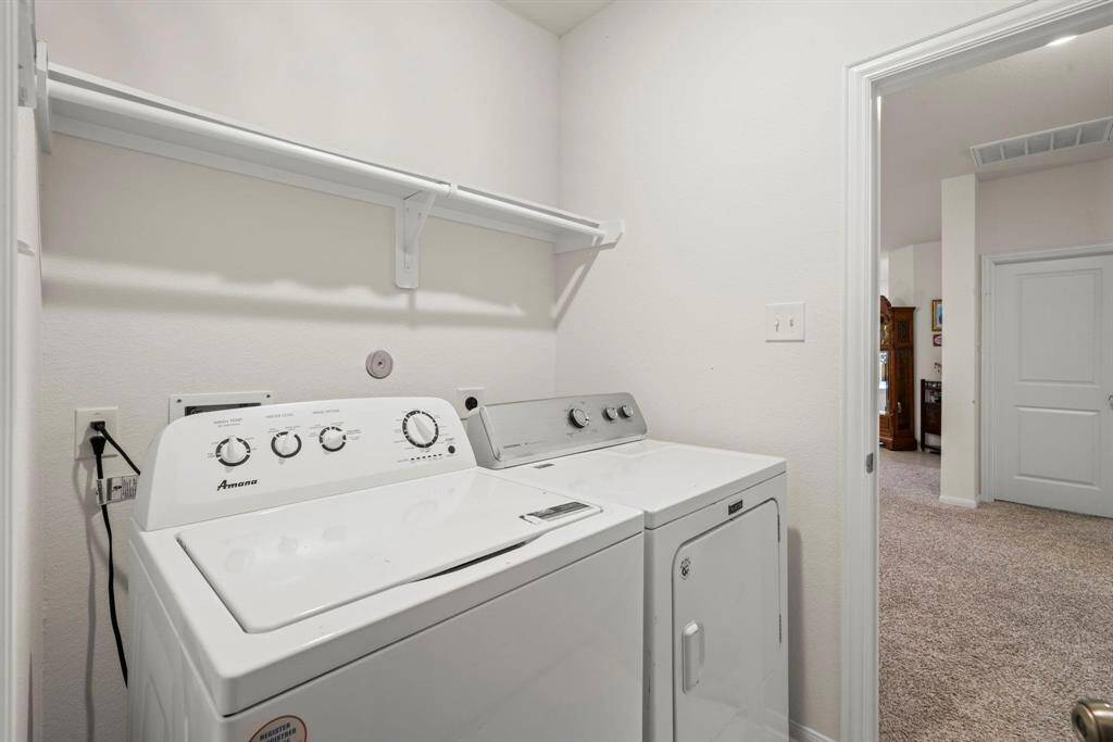 Compact laundry area with washer and dryer, overhead shelf, and open entry to  the house.