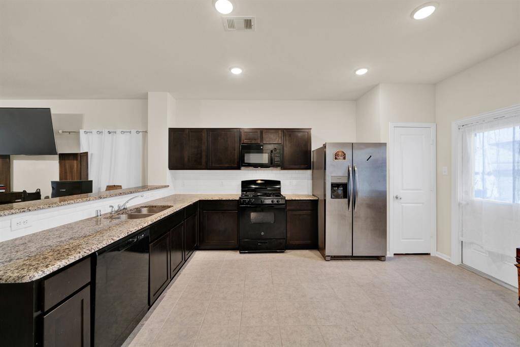 This spacious kitchen features dark cabinetry, granite countertops, and modern stainless steel appliances, offering a sleek and functional cooking space.