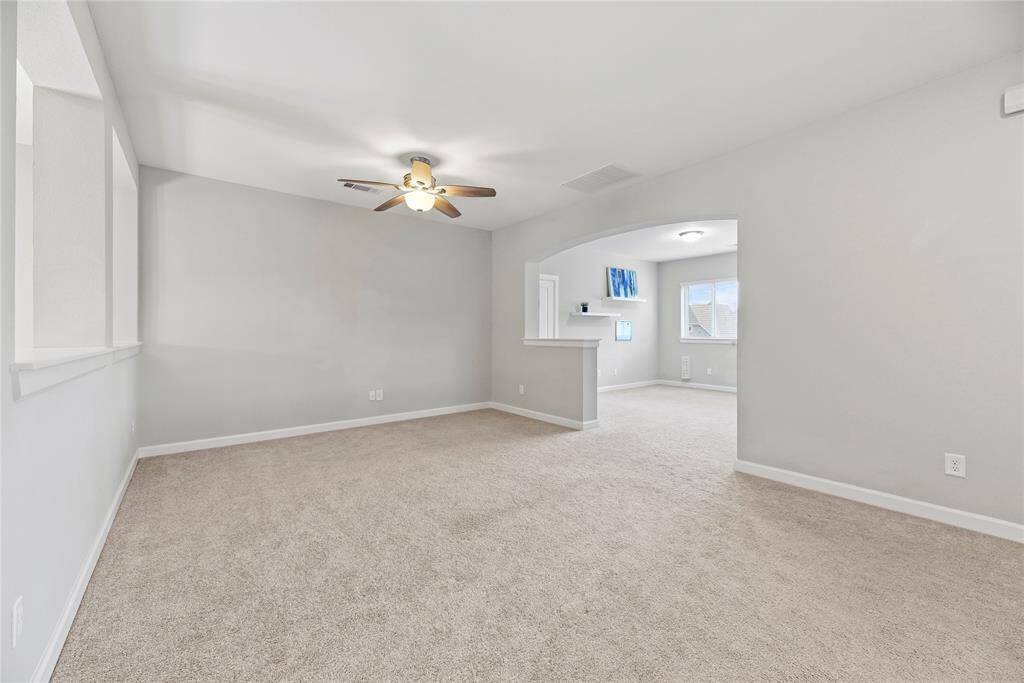 Upstairs living area that can be used as a game room or playroom with a ceiling fan. There's an open archway leading to a bright adjacent room with a window and built-in shelves, creating a seamless flow between spaces.