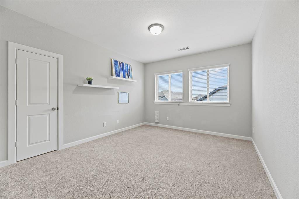 Bright, spacious room featuring two large windows for natural light. Includes a ceiling light, attic access door to what could be a Texas built out basement, and wall-mounted shelves for added storage or decor.