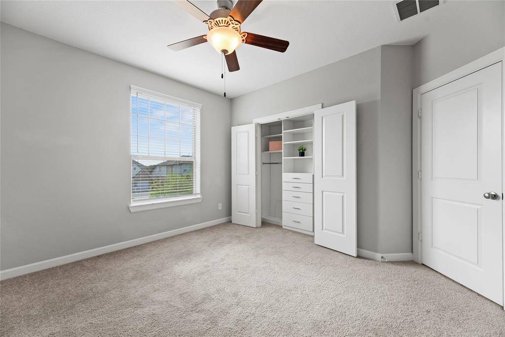 This bright bedroom features  a ceiling fan, and a large window for natural light and includes a spacious closet with built-in shelves and storage.
