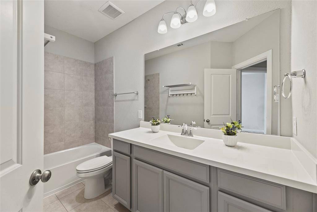 This bathroom features a modern design with a sleek vanity with plenty of storage and counter space and includes a bathtub with tiled walls and neutral tones.
