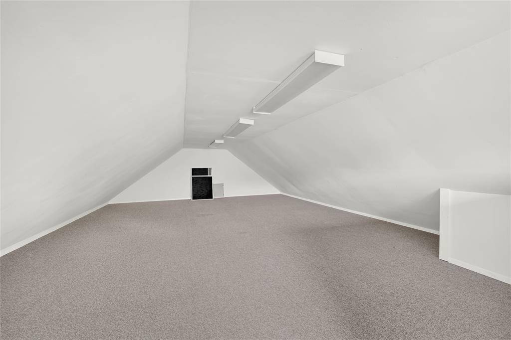 Garage Loft - carpeted space with sloped ceilings and ample overhead lighting, perfect for storage or conversion into a cozy living space.