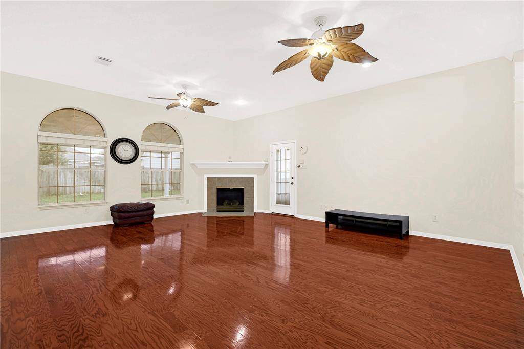 Spacious living room with polished hardwood floors, a central fireplace, and large arched windows offering plenty of natural light. The room features ceiling fans and neutral walls, creating a warm and inviting atmosphere.