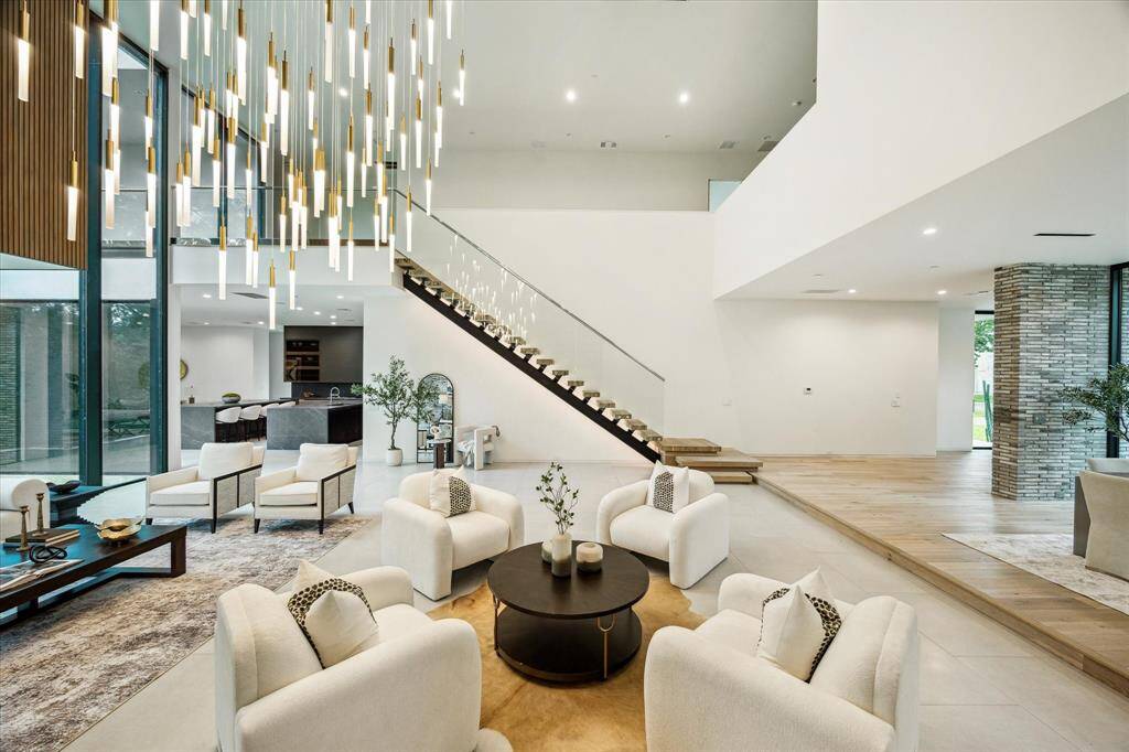 The living room showcases a striking staircase with sleek glass railings and floating wood treads, creating a sculptural centerpiece that gracefully ascends to the second floor.