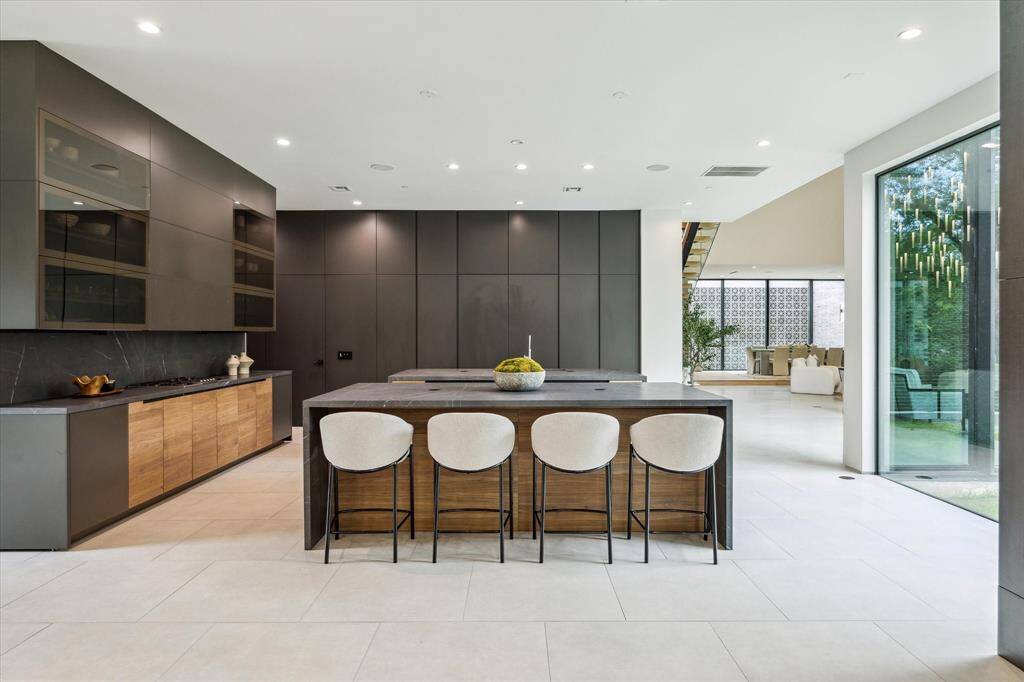The kitchen features custom Poliform Alea cabinetry in a striking combination of Matt Lacquer Rocia, Black Elm Wood, Walnut Wood, and Glossy Bronzed Glass, perfectly complemented by Moderno Porcelain countertops in Matte Pietra Gray. Elite Gaggenau and Miele appliances complete this gourmet space, offering both luxury and functionality.
