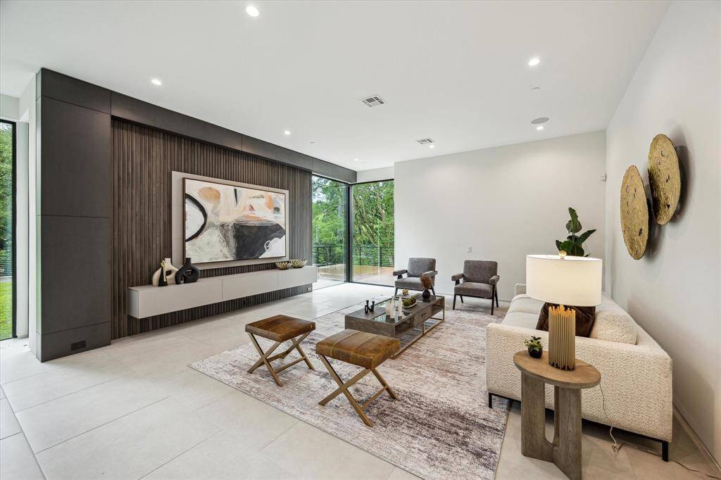 The inviting family room features 32"x32" Belgian Bluestone tile flooring by La Nova, an Innowood accent wall, and custom lighting that frames the TV wall, while a door offers direct access to the serene back patio for effortless indoor-outdoor living.