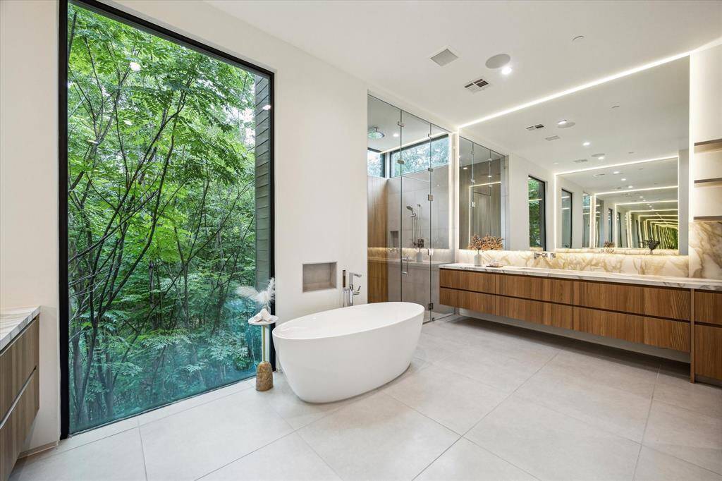 The picturesque outdoor views offer lush green scenery, creating a serene backdrop as you get ready for the day or unwind in the evening. Inside, the primary bathroom features a Cheviot Seville undermount sink, a Poliform vanity in melamine elm, and countertops of Moderno porcelain in Matte Oro White. The shower and accent walls are beautifully finished with Innowood in Tasmanian Oak, adding warmth and elegance to this tr