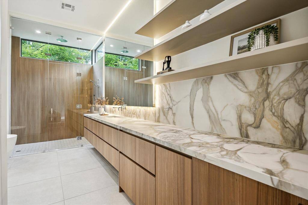 The luxurious primary bathroom is a serene retreat, featuring a Victoria + Albert freestanding tub, wall-mounted faucet and tub filler, and a spacious walk-in shower equipped with a Dornbracht Lulu shower set, ceiling-mounted rain shower, and MEM controls. Dual water closets provide privacy, while a Poliform vanity in melamine elm with Moderno porcelain countertops in Matte Oro White adds refined elegance. An undercounter refrigerator elevate comfort and convenience in this spa-like sanctuary.