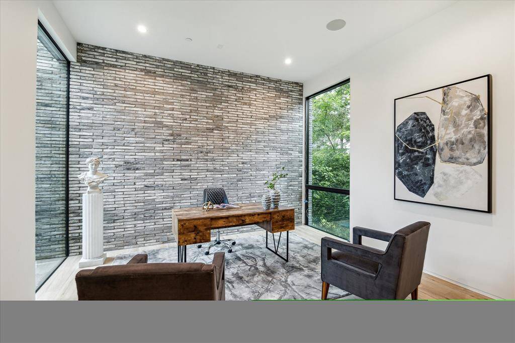 The conveniently located first-floor study is finished with Belgian Bluestone tile by La Nova and features windows that overlook lush natural landscaping, providing a peaceful atmosphere. A striking brick accent wall adds texture and character, while easy access to the nearby powder bathroom enhances the room's functionality.