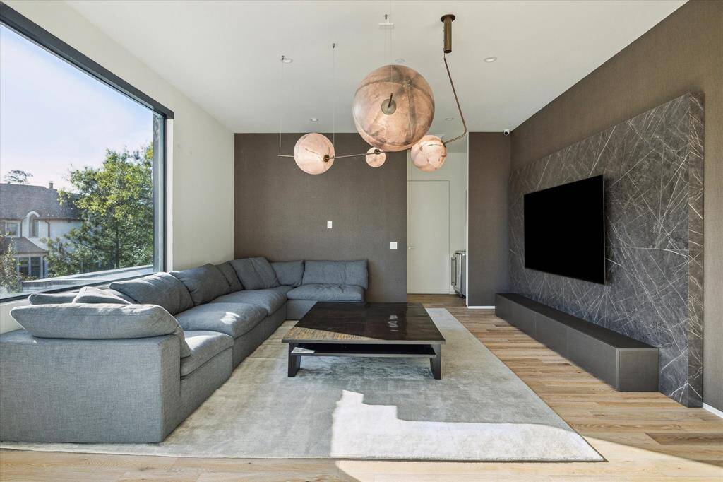 The game room features stunning Maxwell White Oak hardwood flooring, remote-controlled shades for ease and comfort, and is pre-wired for chandelier lighting to enhance the space. An accent wall with Innowood detailing adds texture and warmth, while large windows provide picturesque views of the front lawn.