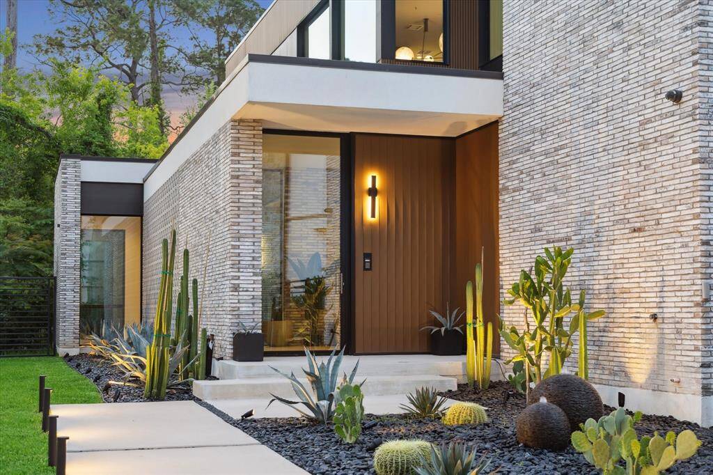 A lighted path welcomes you to the striking entry, where a custom glass-paneled front door is framed by handcrafted brick and sustainable Innowood accents. Thoughtful exterior lighting highlights the home’s modern lines and architectural detail. This stunning entrance sets the tone for the sophisticated design found throughout.