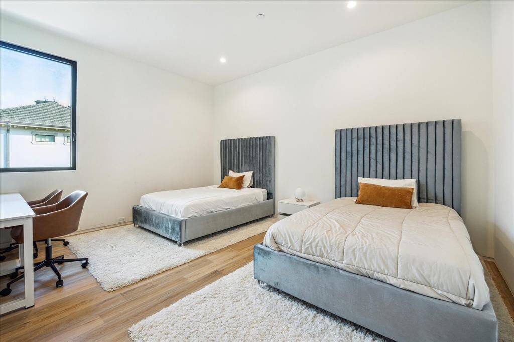 The guest bedroom is finished with White Oak wood floors, neutral wall paint, and a window that offers a view of the motor court. It also includes an ensuite bathroom and a custom closet, combining comfort and convenience for guests.