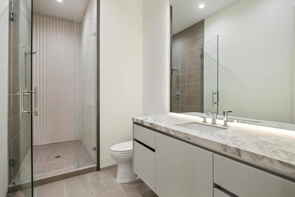 The guest bathroom features La Nova floor tile, a walk-in shower with polished nickel finishes, and a custom backlit mirror, creating a sleek and modern atmosphere. Ample vanity space provides both functionality and style, making the room both practical and inviting.
