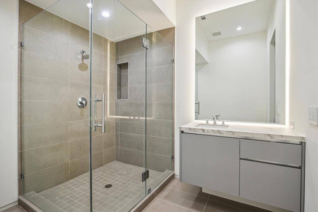 The guest bathroom features a walk-in shower with a built-in shower niche, polished nickel hardware, and a vanity with custom backlighting, creating a sleek and functional space with a touch of elegance.