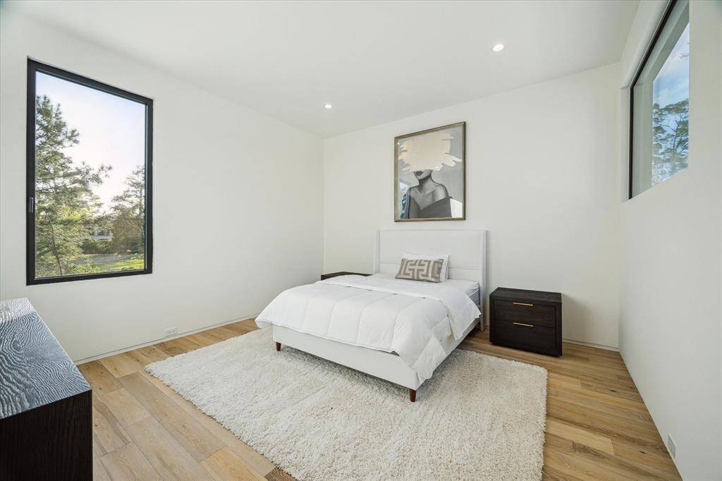 The guest bedroom is brightened by recessed can lights and features neutral wall paint, creating a calming atmosphere. It also includes a walk-in closet and engineered hardwood floors, offering both style and practicality.