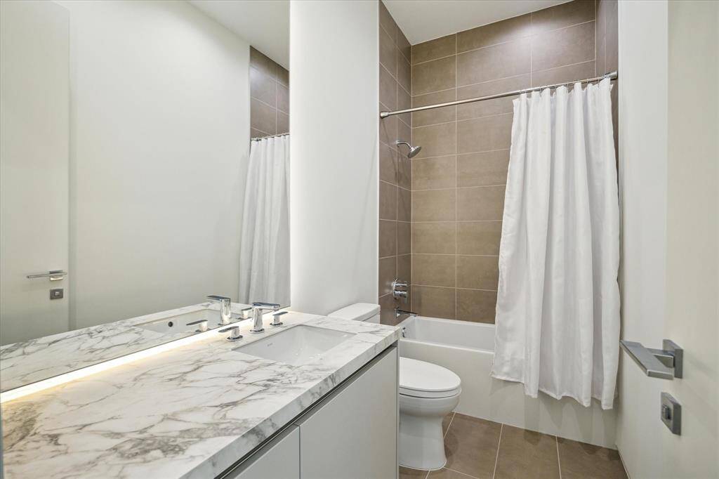 This guest bathroom is conveniently located off the guest bedroom and is easily accessible from the game room. It features under-counter storage, a Rohl shower faucet, a Toto commode, and custom backlighting, offering both functionality and a modern touch.