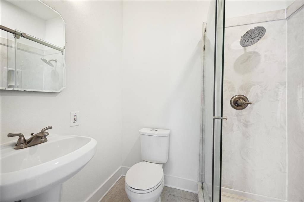 Secondary bathroom with tile floors, sconce lighting, pedestal sink and a walk-in shower.