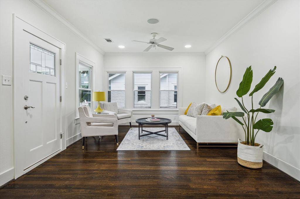 Step into the sunlit living room, where original charm meets modern comfort. Crisp white walls, rich hardwood floors, and oversized windows create a serene and inviting space—perfect for entertaining or relaxing.