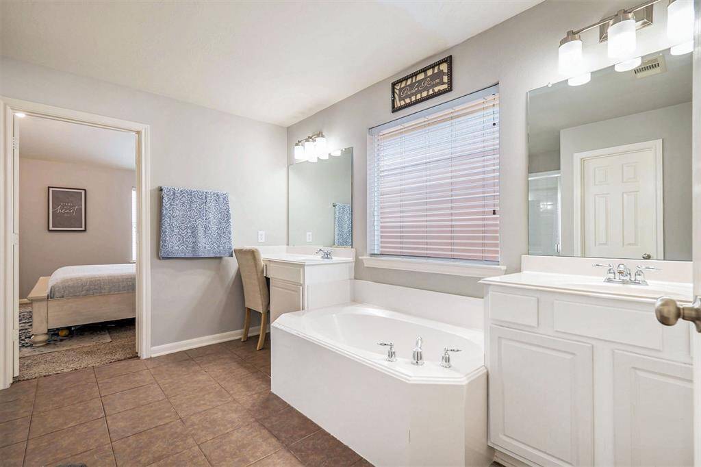 Primary bathroom features dual vanities, a relaxing soaking tub, and a glass standing shower.