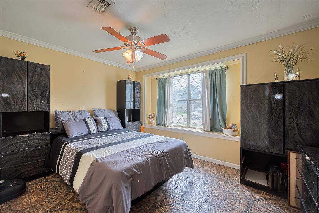 Cozy bedroom with a large window providing natural light, featuring a ceiling fan, stylish dark wood furniture, and decorative tile flooring