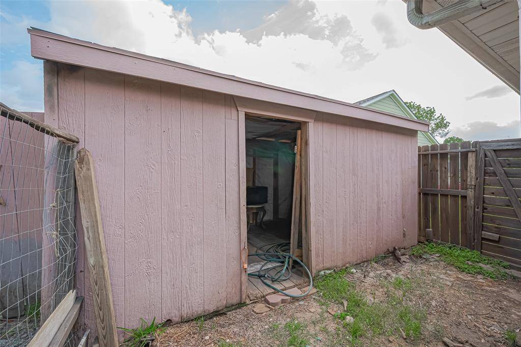 Weathered wooden shed with an open door, located in a fenced backyard area. The surrounding ground is bare with patches of grass. Ideal for storage or a small workshop.