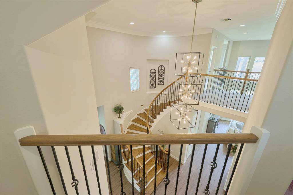 Discover a spacious, elegant interior featuring a striking curved staircase with wooden steps and wrought iron railings. Enjoy modern chandelier lighting and an open layout with views of multiple living areas.
