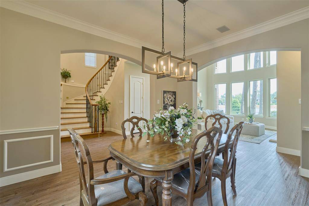 Discover a sophisticated dining area featuring warm LVP floors, a chic chandelier, and seamless views into the spacious living room and staircase.