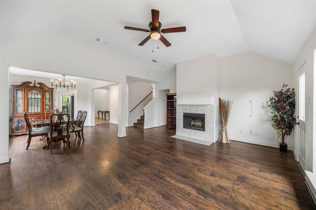 Another view of the spacious family and dining area features hardwood floors, a cozy fireplace, and high ceilings with a ceiling fan. It opens into the dining room, creating a warm and inviting atmosphere.