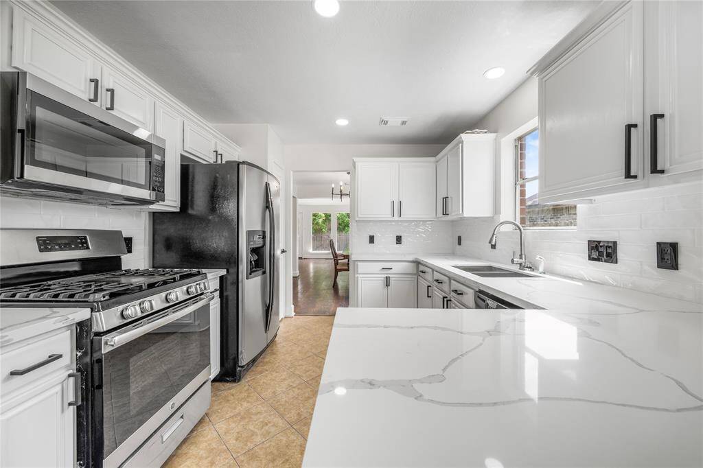This modern kitchen features sleek white cabinetry, stainless steel appliances, and elegant marble countertops. It offers ample natural light and a spacious layout, perfect for cooking and entertaining.