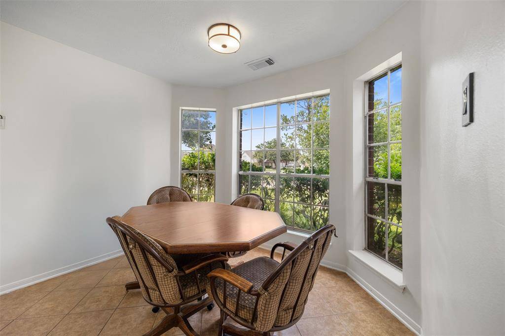 This bright dining area features large windows with garden views, neutral tile flooring, and a cozy setup with a round table and wicker chairs, perfect for intimate gatherings.
