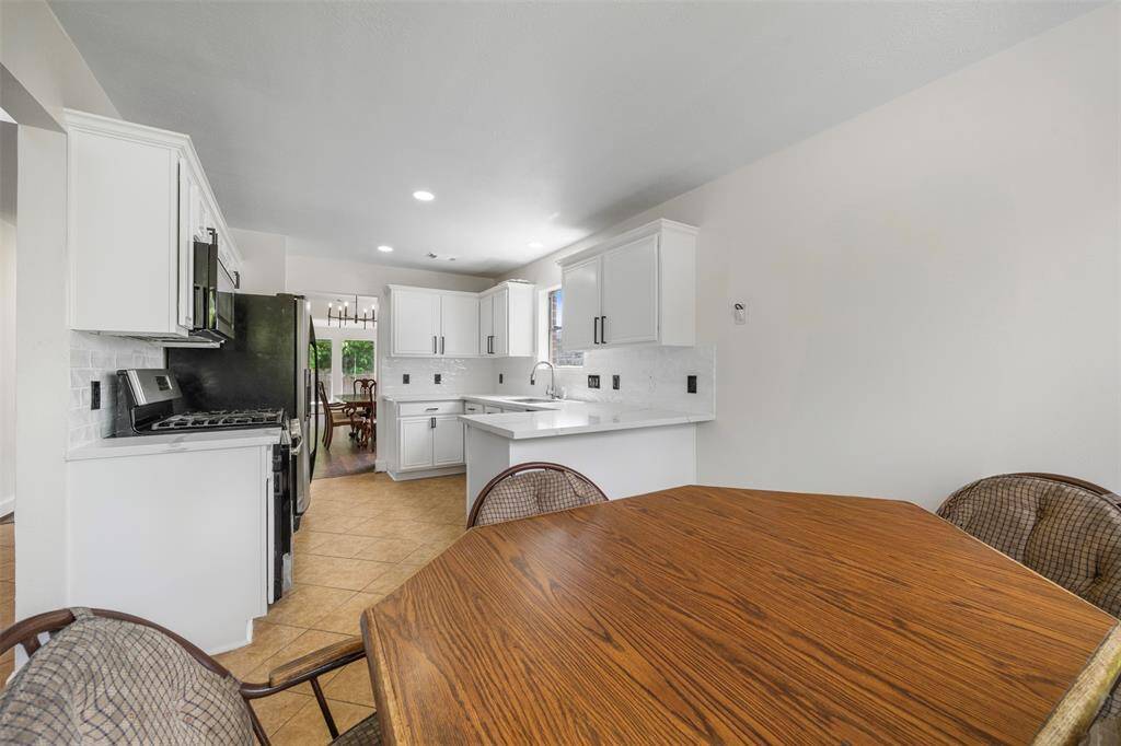 This photo showcases a bright kitchen with white cabinetry, modern stainless steel appliances, and tiled flooring. There's a cozy dining area creating a welcoming space for meals.