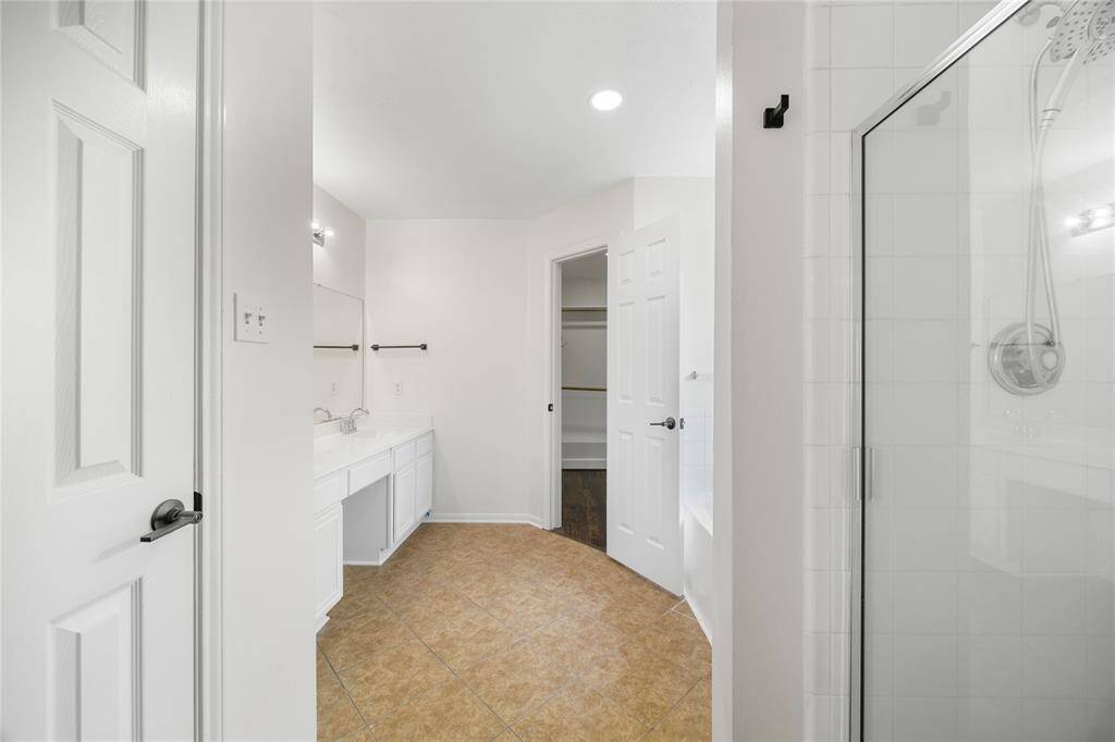 This photo showcases a bright, modern bathroom with a glass-enclosed shower, dual sinks, and a spacious walk-in closet. The neutral color palette and tiled flooring add a clean, contemporary feel.