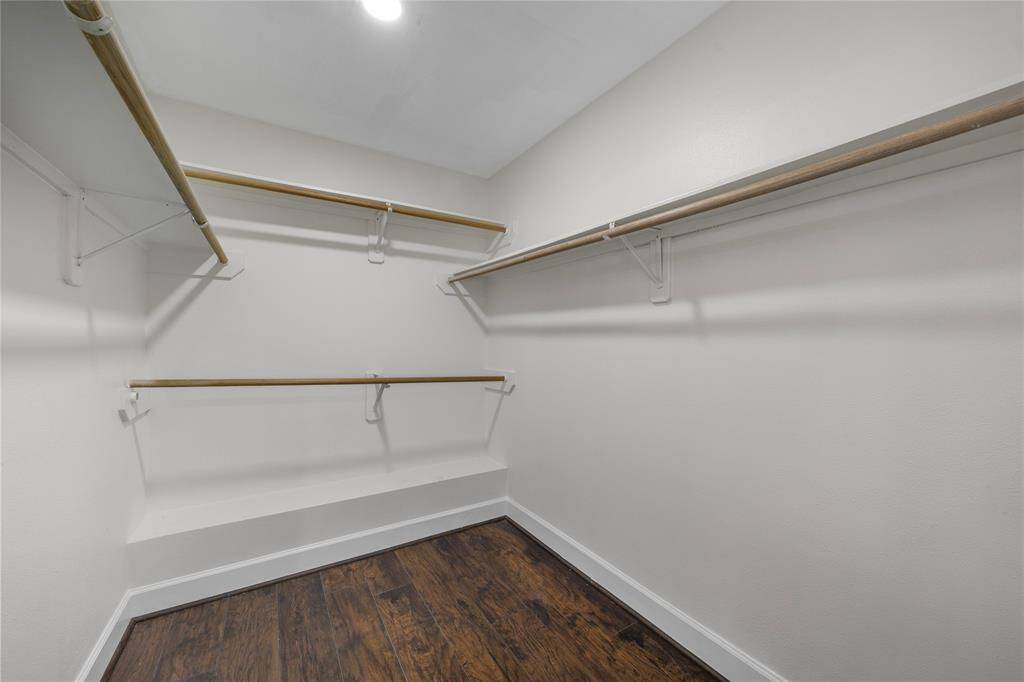 This photo shows a spacious walk-in closet with multiple wooden hanging rods and a built-in bench, featuring hardwood floors and bright lighting.