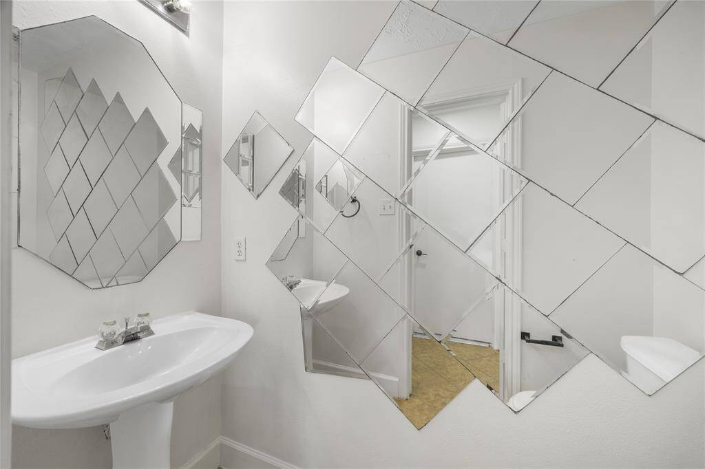 Power room features a unique geometric mirror design on the walls, a sleek pedestal sink, and a minimalist aesthetic with bright lighting, creating a modern and spacious feel.