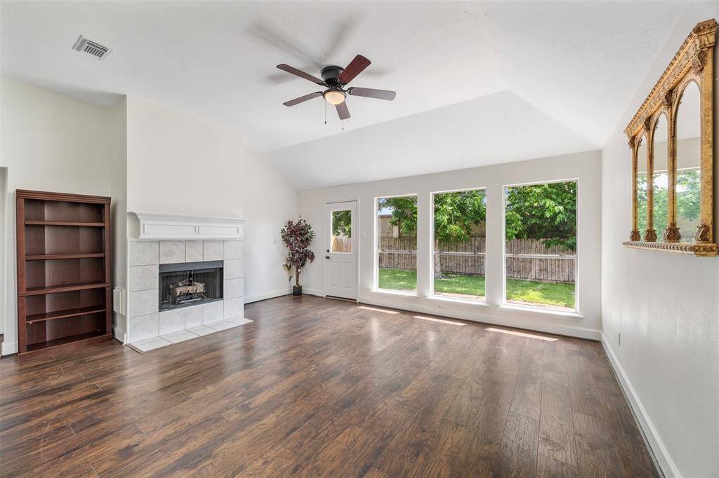 Bright family room with large windows, hardwood floors, and a cozy fireplace. Features a high ceiling with a fan offering a view of the backyard through the door and windows.