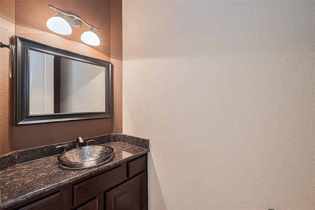 The downstairs powder room has a sunken vessel bowl sink and a framed mirror. Also has a furniture piece vanity, granite countertop and Moen oil-rubbed bronze hardware.